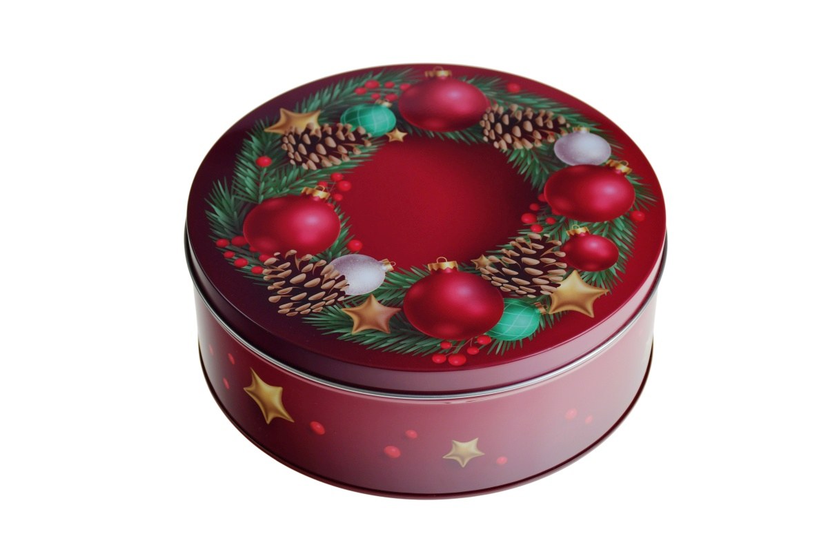 Boîte en fer blanc ronde fermée avec motif de Noël, fond rouge avec branches de sapin, pommes de pin, étoiles dorées et boules rouges, photographiée sur fond neutre.