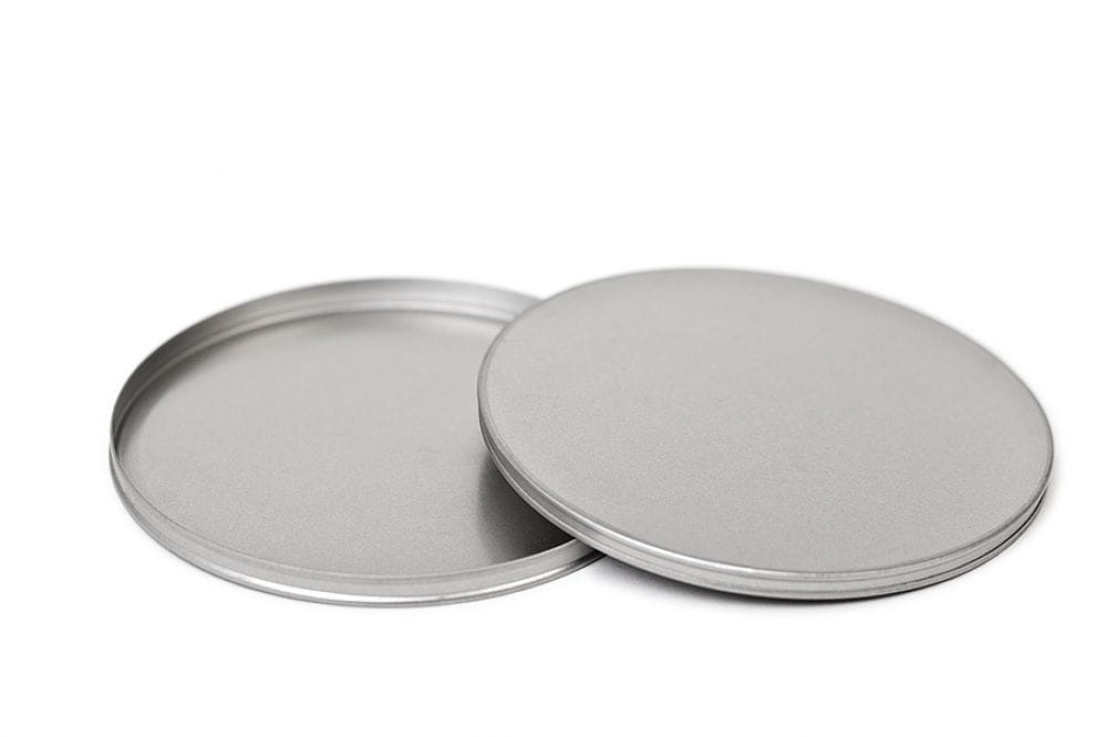 Boîte en fer blanc ronde ouverte avec couvercle emboîtant retiré, couleur argent, fond neutre.