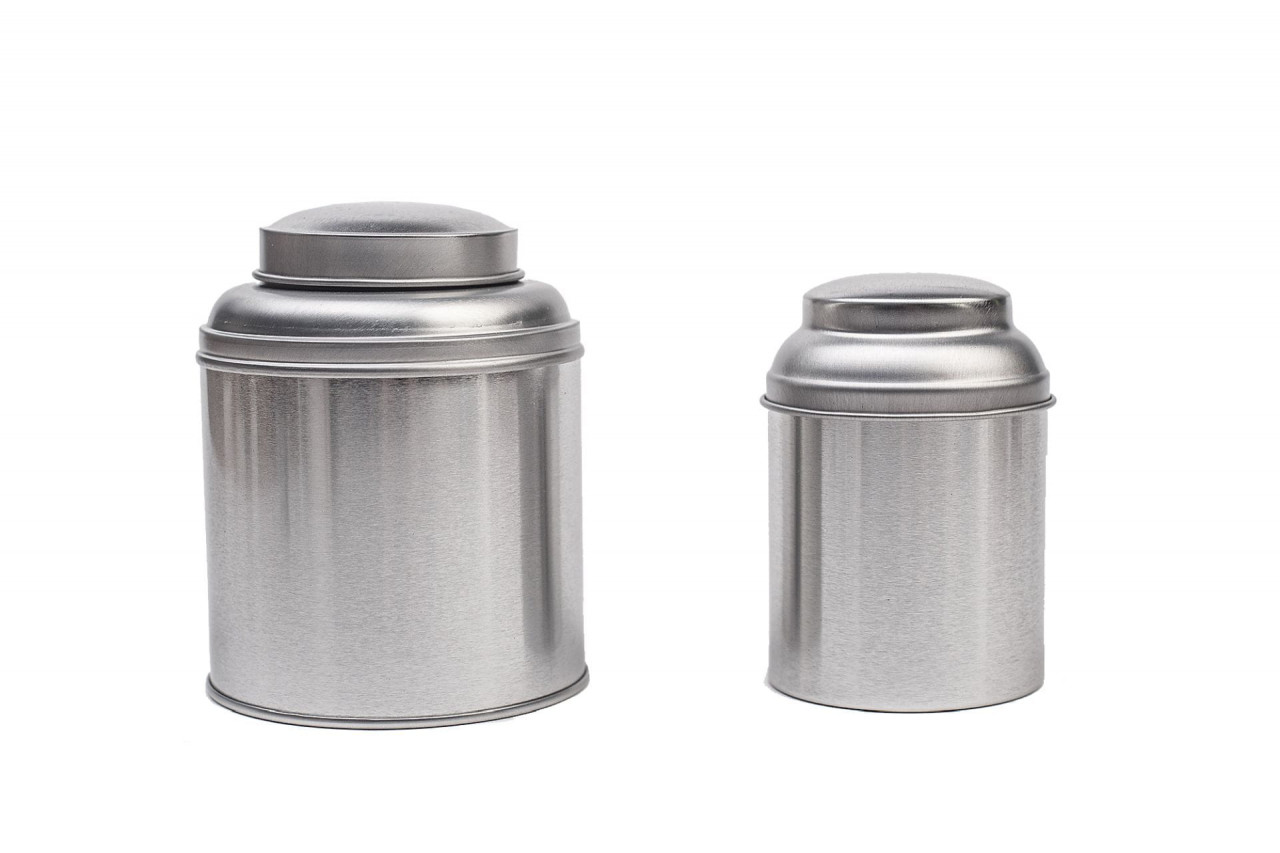 Deux boîtes à thé rondes fermées en métal couleur argent avec couvercle à arôme, une grande et une petite boîte côte à côte sur fond blanc.