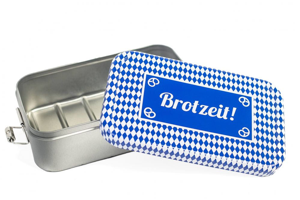Boîte à lunch carrée ouverte en métal de couleur argent avec couvercle retiré au motif losange bleu et blanc et inscrit « Brotzeit! », intérieur avec compartiments, sur fond blanc.