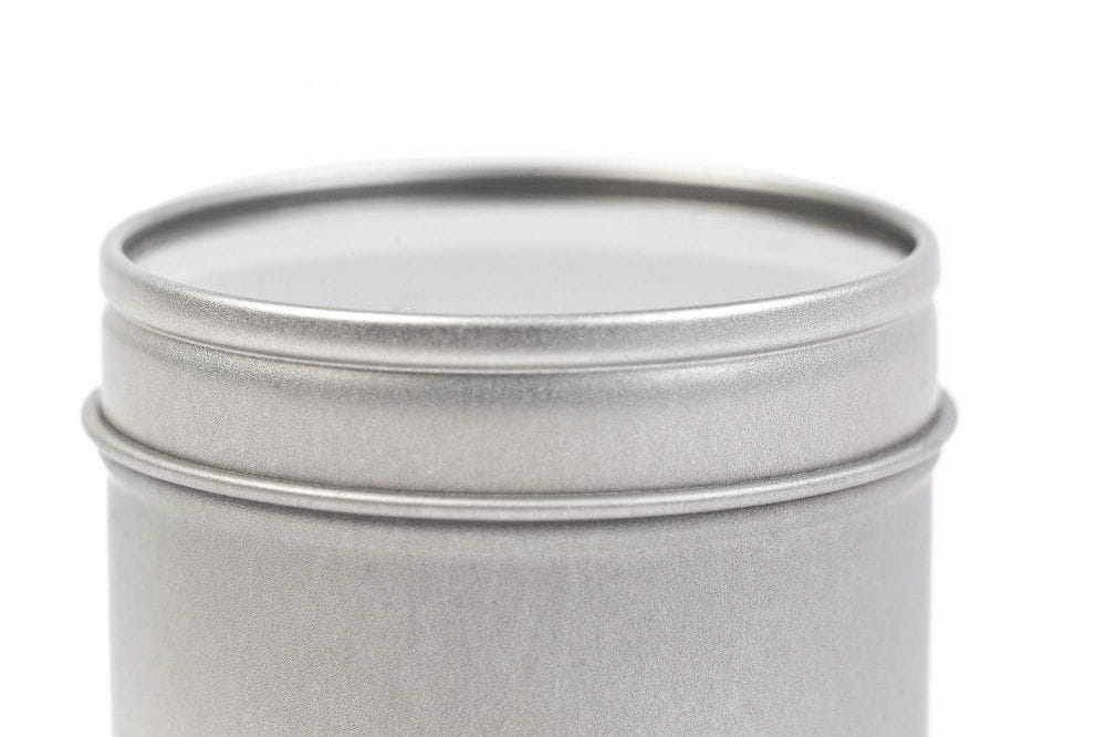 Boîte en fer blanc ronde fermée en métal argenté avec couvercle et fenêtre de visualisation intégrée, photographiée sur fond blanc.