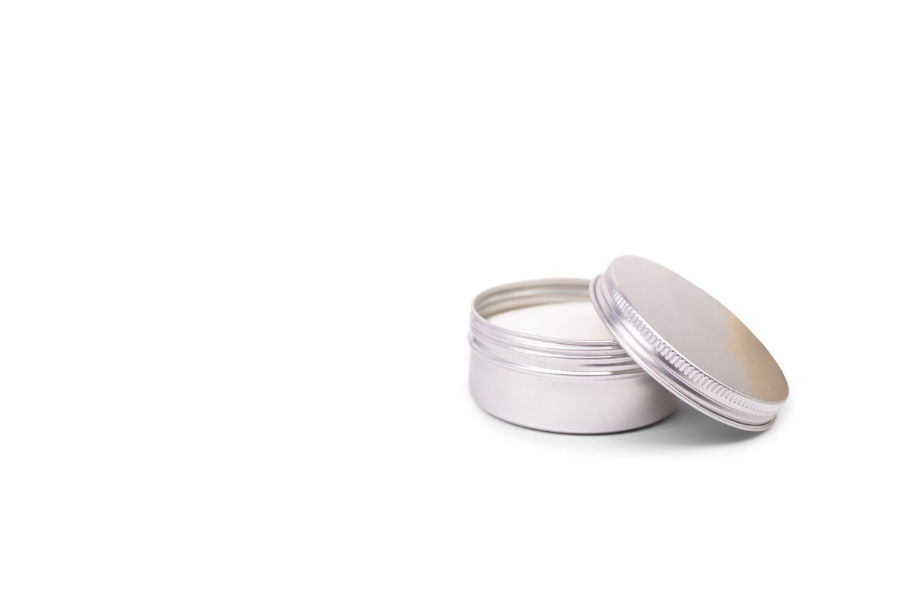 Boîte cosmétique en aluminium argenté ouverte avec volume de 130 ml, remplie de crème blanche, photographiée sur fond blanc. Le couvercle repose légèrement sur la boîte.