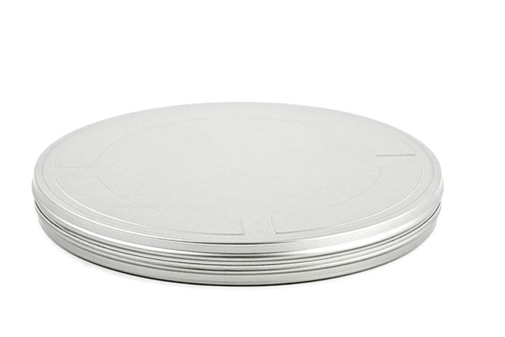 Boîte de film ronde fermée en métal argenté avec couvercle emboîtant plat, photographiée sur fond blanc.