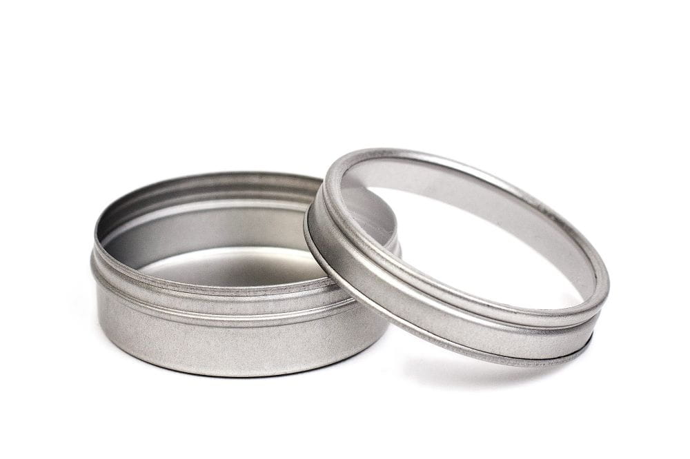 Boîte à épices ronde ouverte en métal couleur argent avec couvercle à fenêtre de visualisation retiré, photographiée sur fond blanc.
