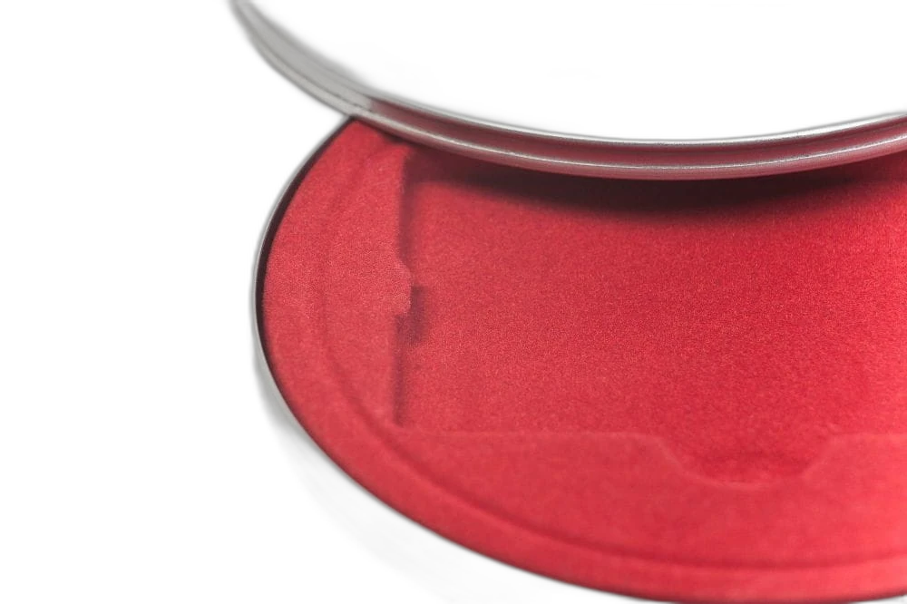 Vue détaillée d'une boîte métallique ronde couleur argent avec couvercle partiellement ouvert, intérieur doublé de velours rouge.