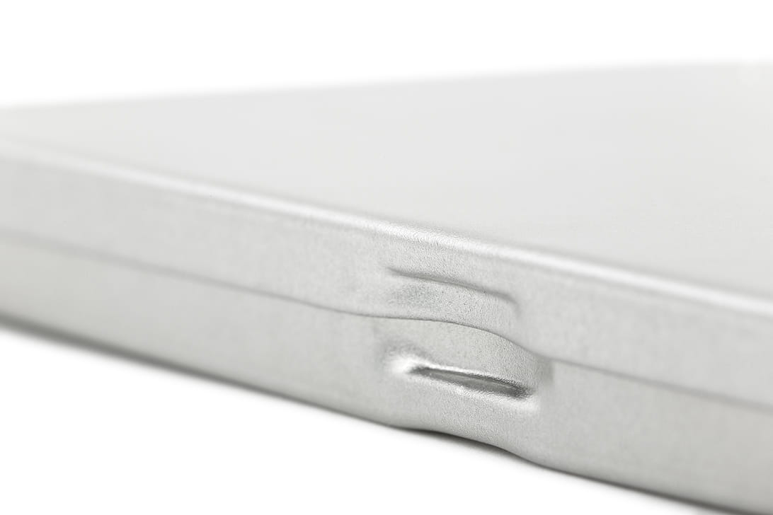 Détail rapproché d'une boîte métallique carrée fermée en tôle couleur argent avec fermeture à clip visible, sur fond neutre.