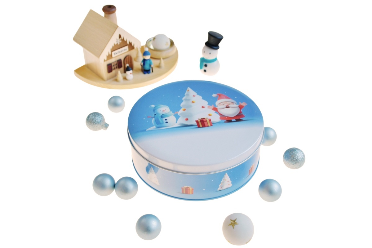 Boîte métallique ronde fermée avec motif hivernal sur fond bleu, représentant un Père Noël, un bonhomme de neige, un sapin et un cadeau, photographiée sur fond blanc.