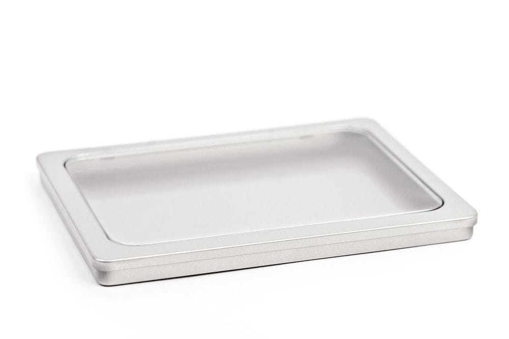 Boîte métallique DIN-A5 fermée en fer blanc de couleur argentée avec fenêtre de visualisation intégrée dans le couvercle, photographiée sur fond blanc.