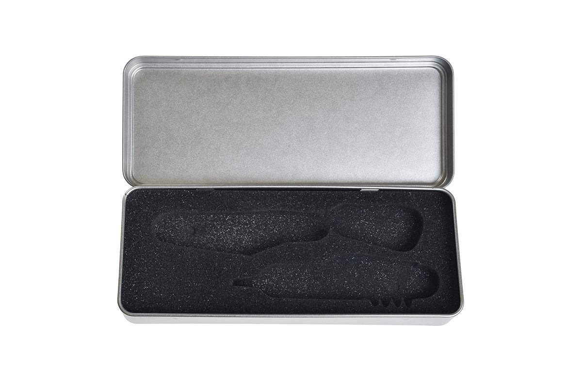 Boîte métallique rectangulaire ouverte avec couvercle amovible, vide, avec insert en mousse noire pour couverts, sur fond blanc.