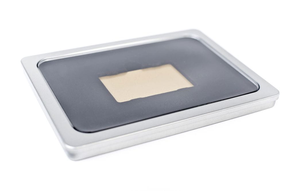 Boîte en fer blanc rectangulaire fermée en métal argenté avec fenêtre de visualisation dans le couvercle et doublure noire, photographiée sur fond neutre.