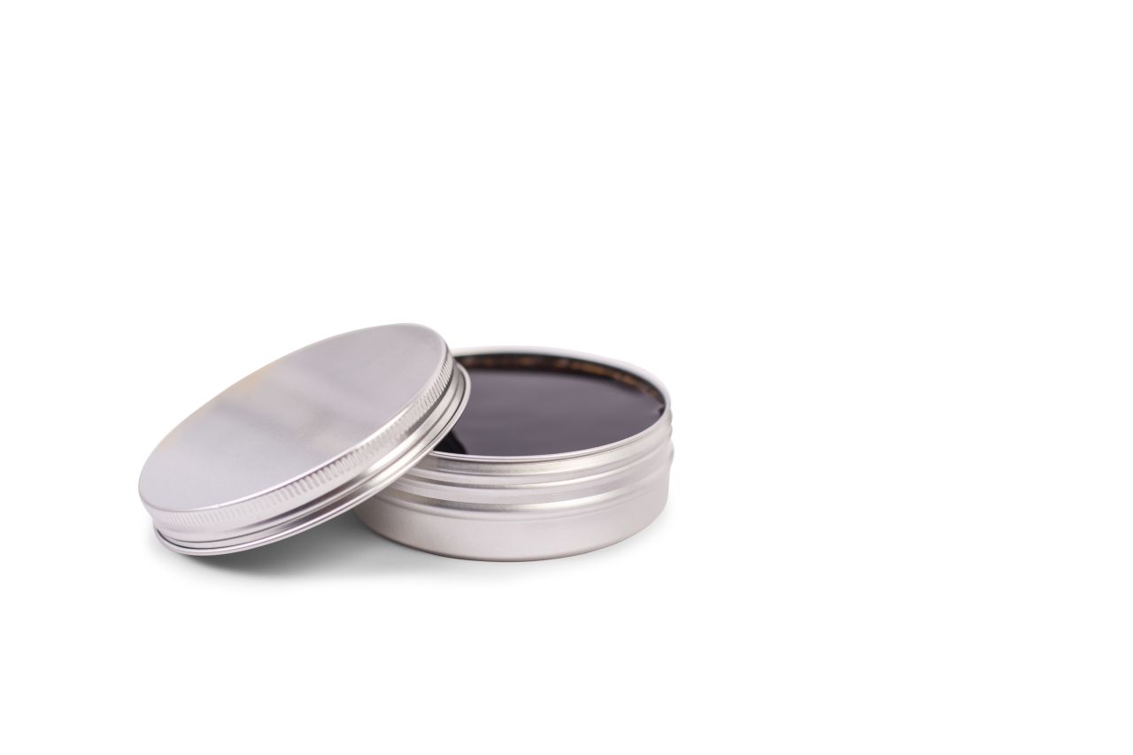 Boîte en aluminium argenté ouverte avec capacité de 125 ml, remplie d'une substance foncée, possiblement huileuse. Le couvercle est légèrement appuyé et le fond est blanc.