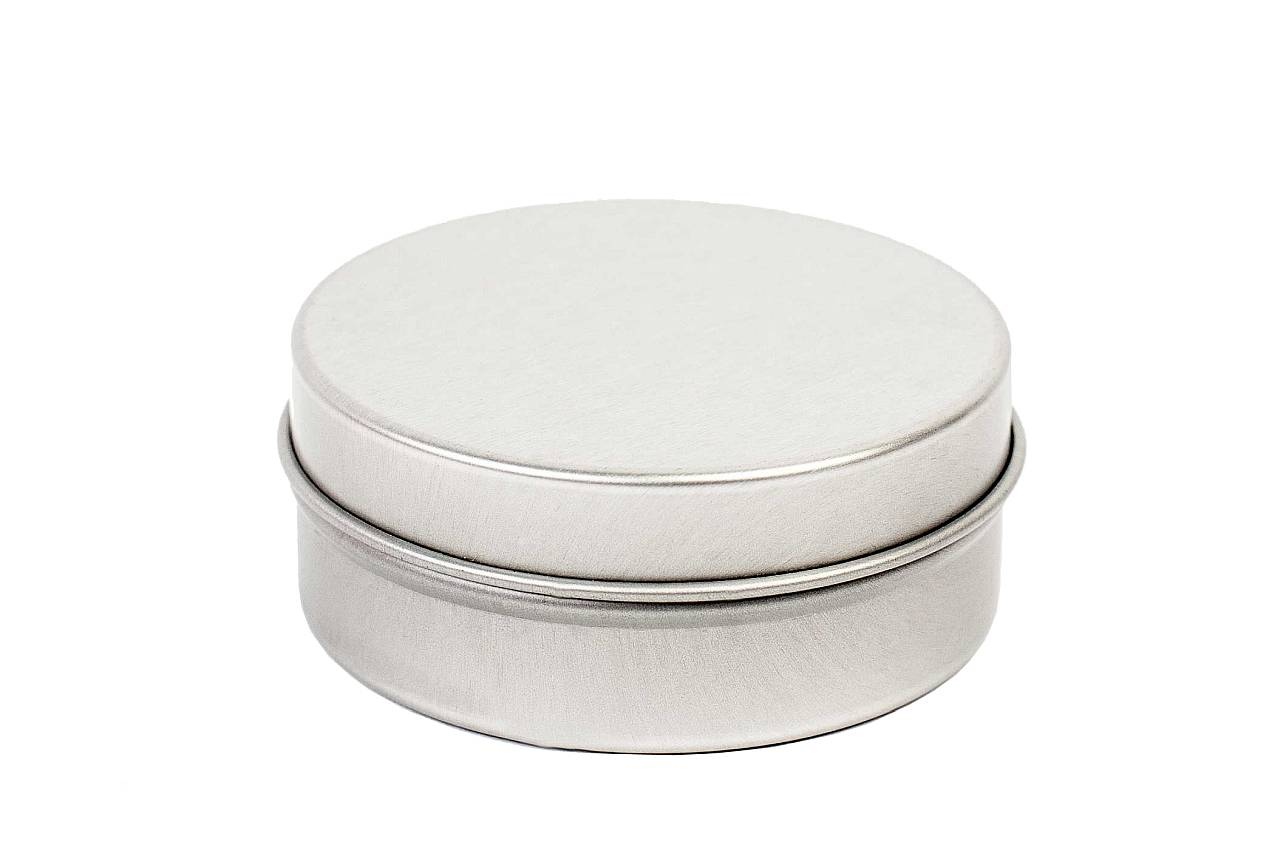 Petite boîte métallique ronde et plate fermée avec couvercle emboîtant sur fond blanc.