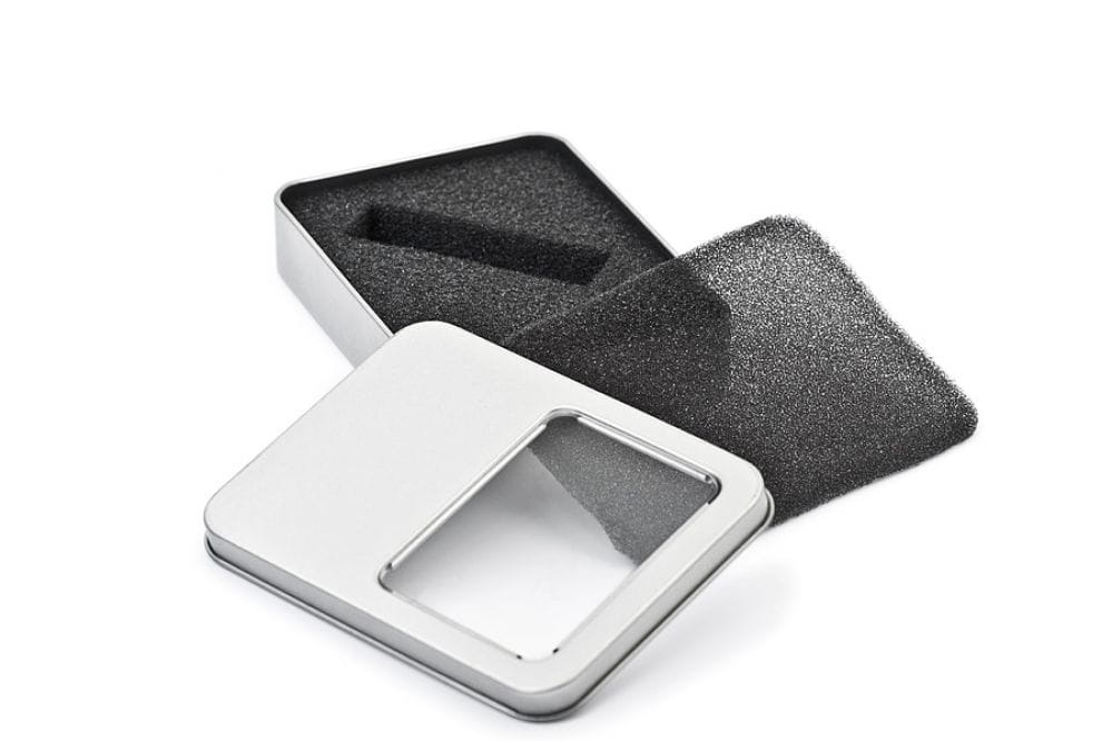 Boîte métallique rectangulaire ouverte couleur argent avec fenêtre de visualisation transparente dans le couvercle, insert en mousse noire pour clé USB, photographiée sur fond blanc.