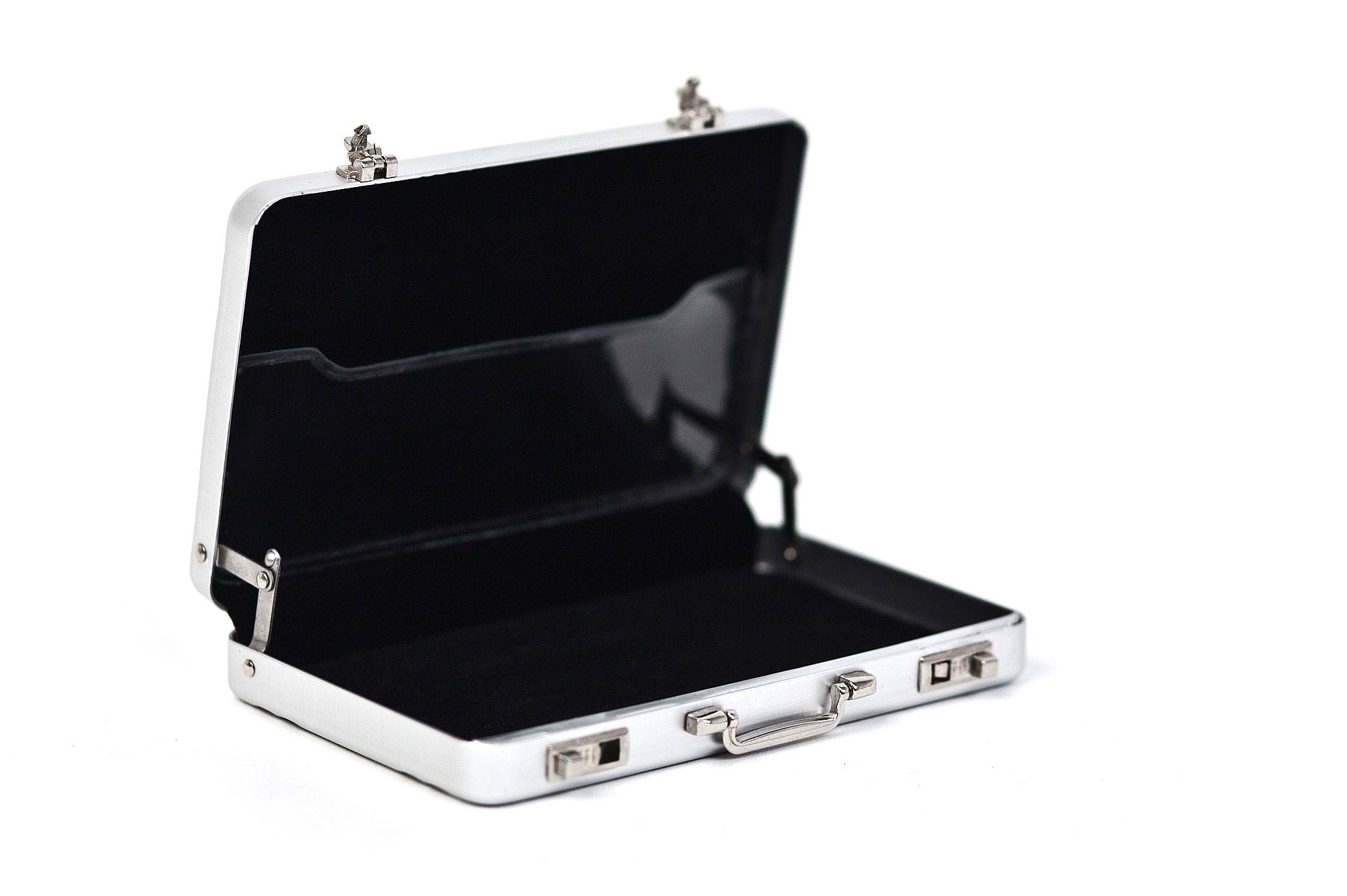 Mini-mallette en aluminium rectangulaire ouverte en argent avec doublure intérieure noire, photographiée sur fond blanc.