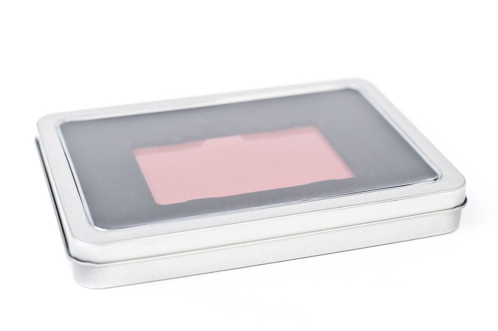 Boîte à bons d'achat rectangulaire fermée en métal argenté avec fenêtre de visualisation transparente dans le couvercle, fond blanc neutre.