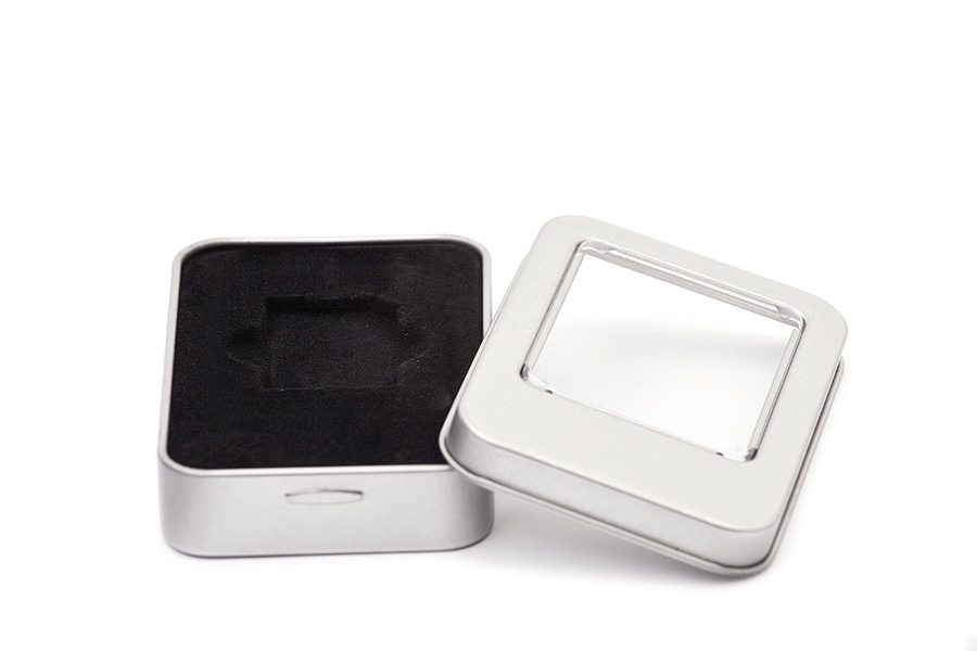 Boîte métallique rectangulaire ouverte en métal couleur argent avec fenêtre de visualisation transparente dans le couvercle et insert noir pour le rangement sécurisé d'une carte SD, photographiée sur fond blanc.