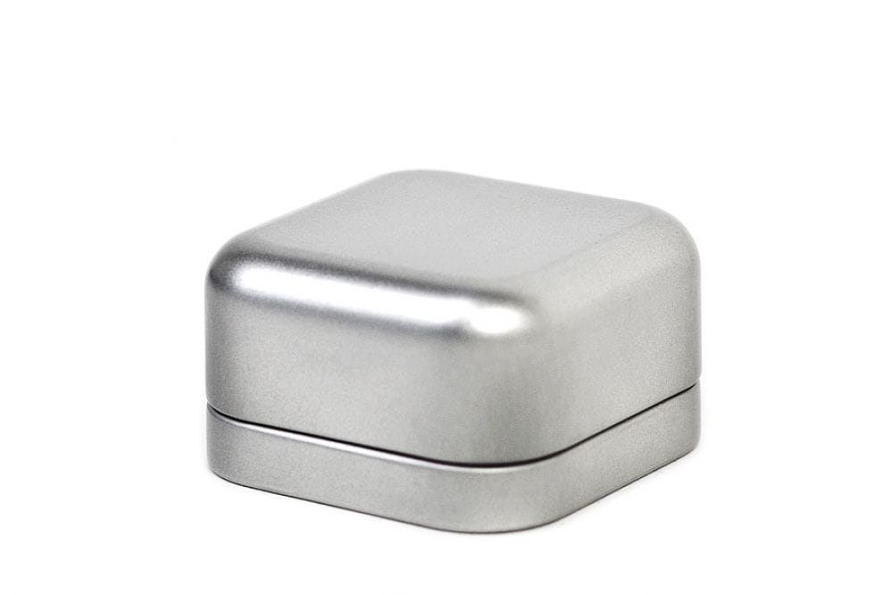 Petite boîte métallique carrée fermée en argent, avec couvercle rapporté, fond blanc neutre.