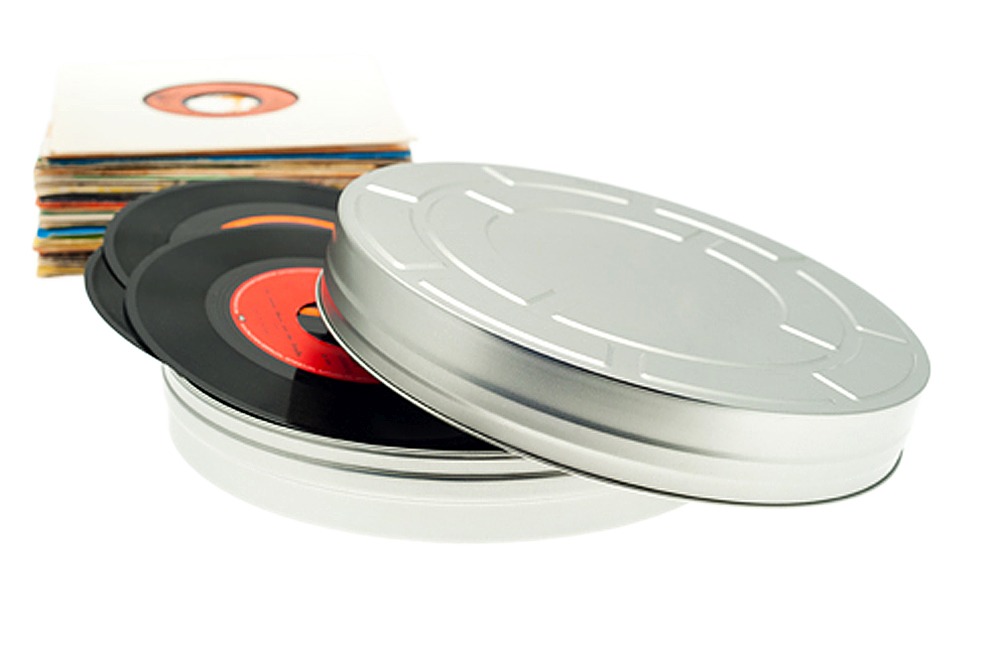 Boîte métallique ronde pour films XL ouverte en métal couleur argent avec couvercle emboîtant retiré, remplie de disques vinyles, accompagnée d'une pile de pochettes de disques, photographiée sur fond blanc.